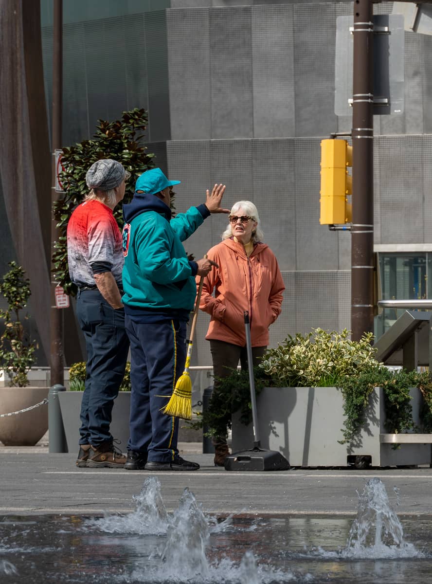 A CCD maintenance staff person gives directions to some people while standing near a fountain.