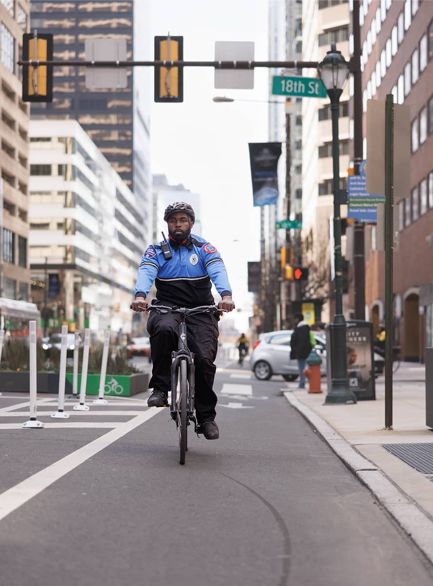 A CCD public safety bike patrol officer, wearing a blue jacket, bike helmets and carrying a 2-way radio, rides his bike down the street.