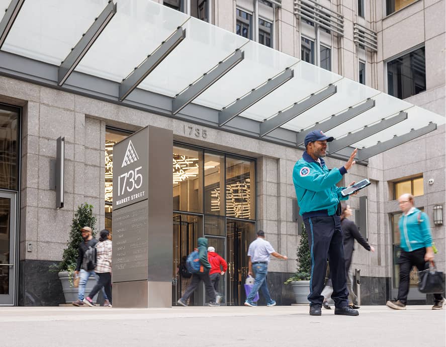 CCD community service representative (CSR for short) safety ambassador wearing a teal jacket, baseball cap and carrying 2-way radio and tablet, giving people brochures.