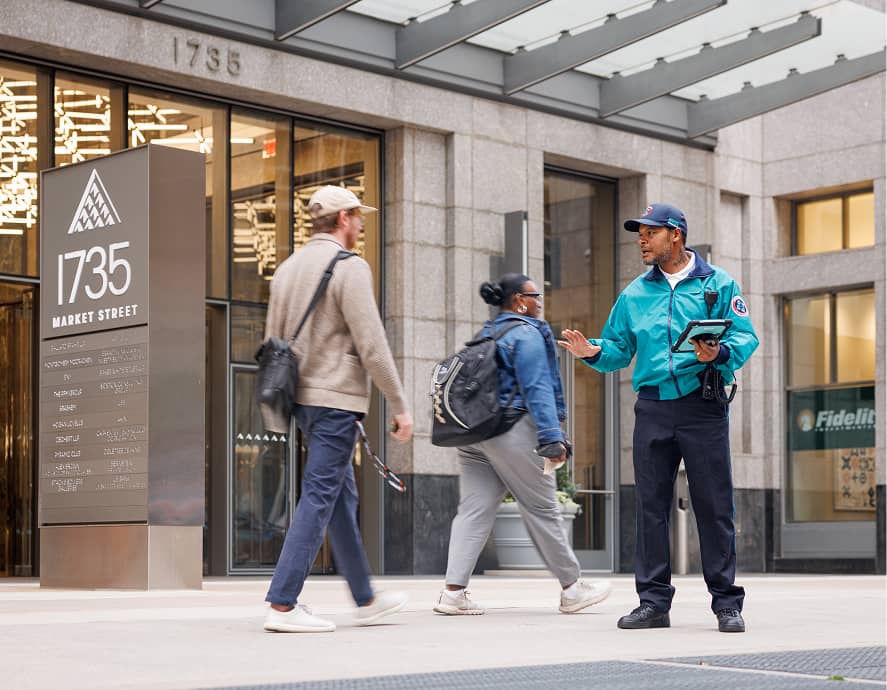 CCD community service representative (CSR for short) safety ambassador wearing a teal jacket, baseball cap and carrying 2-way radio and tablet, giving people brochures.